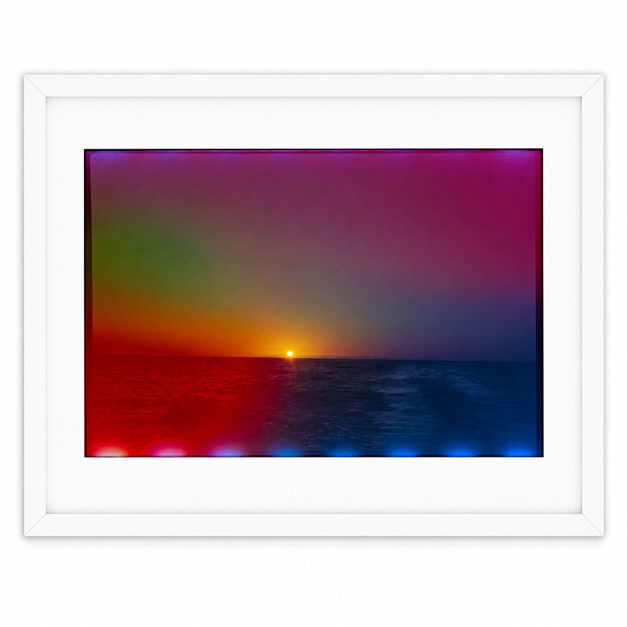 A framed art print featuring a colorful sunset over the ocean, with a white frame and mat, shown against a plain white background.