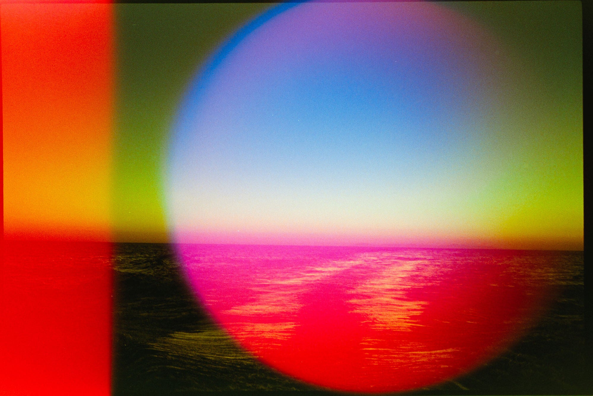 A colorful abstract landscape-style artwork showing a bright blue sky over a magenta and red reflective surface, with green and yellow bands and a large circular gradient overlay.