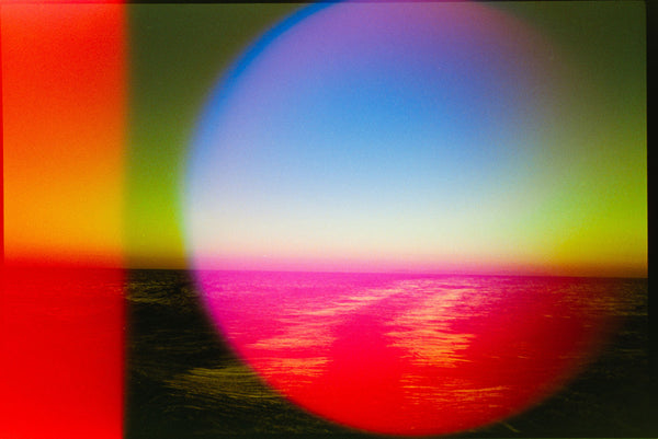 A colorful abstract landscape-style artwork showing a bright blue sky over a magenta and red reflective surface, with green and yellow bands and a large circular gradient overlay.
