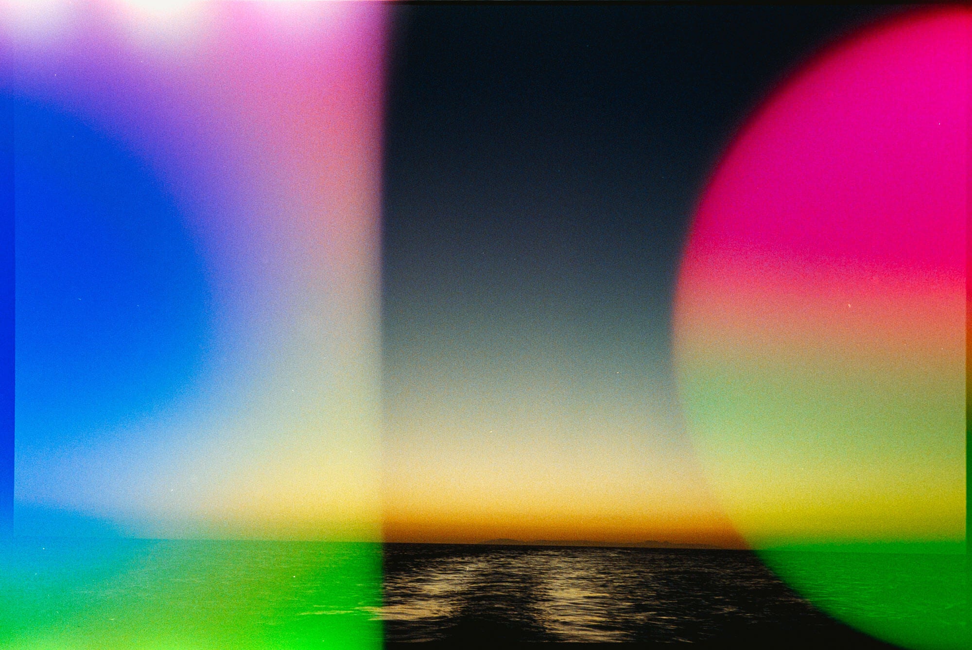 Abstract landscape photograph of a sunset over water, heavily overlaid with colorful circular lens flares in blue, pink, green, and yellow.