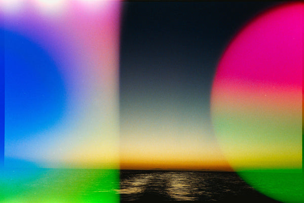 Abstract landscape photograph of a sunset over water, heavily overlaid with colorful circular lens flares in blue, pink, green, and yellow.
