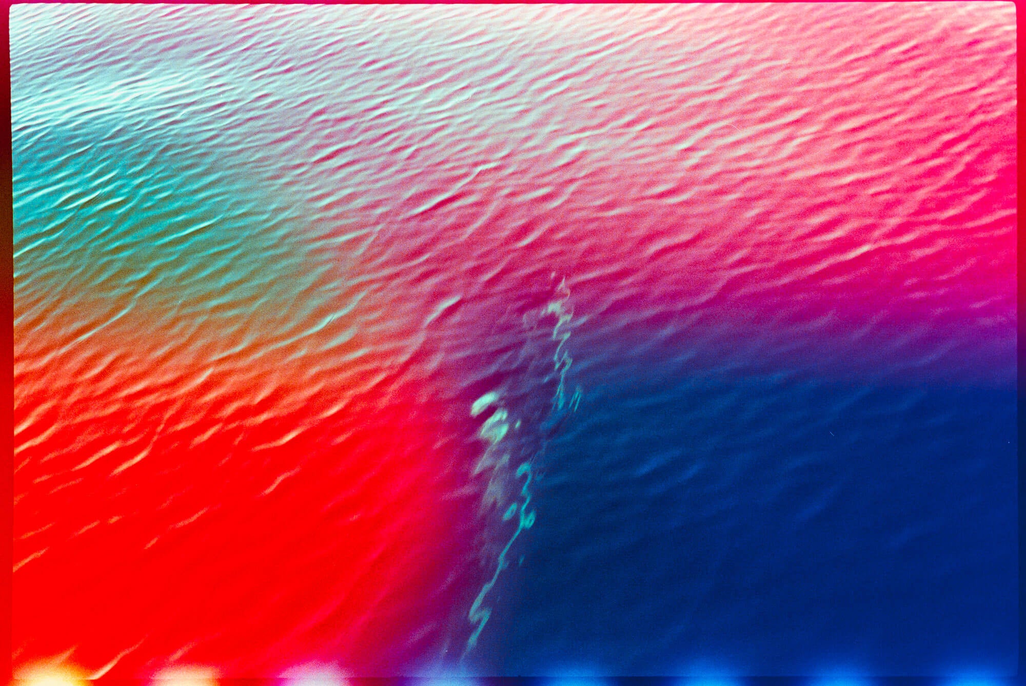 Abstract colorful artwork with rippling texture, showing large areas of red, pink, cyan, and deep blue with small bright light spots along the bottom edge.