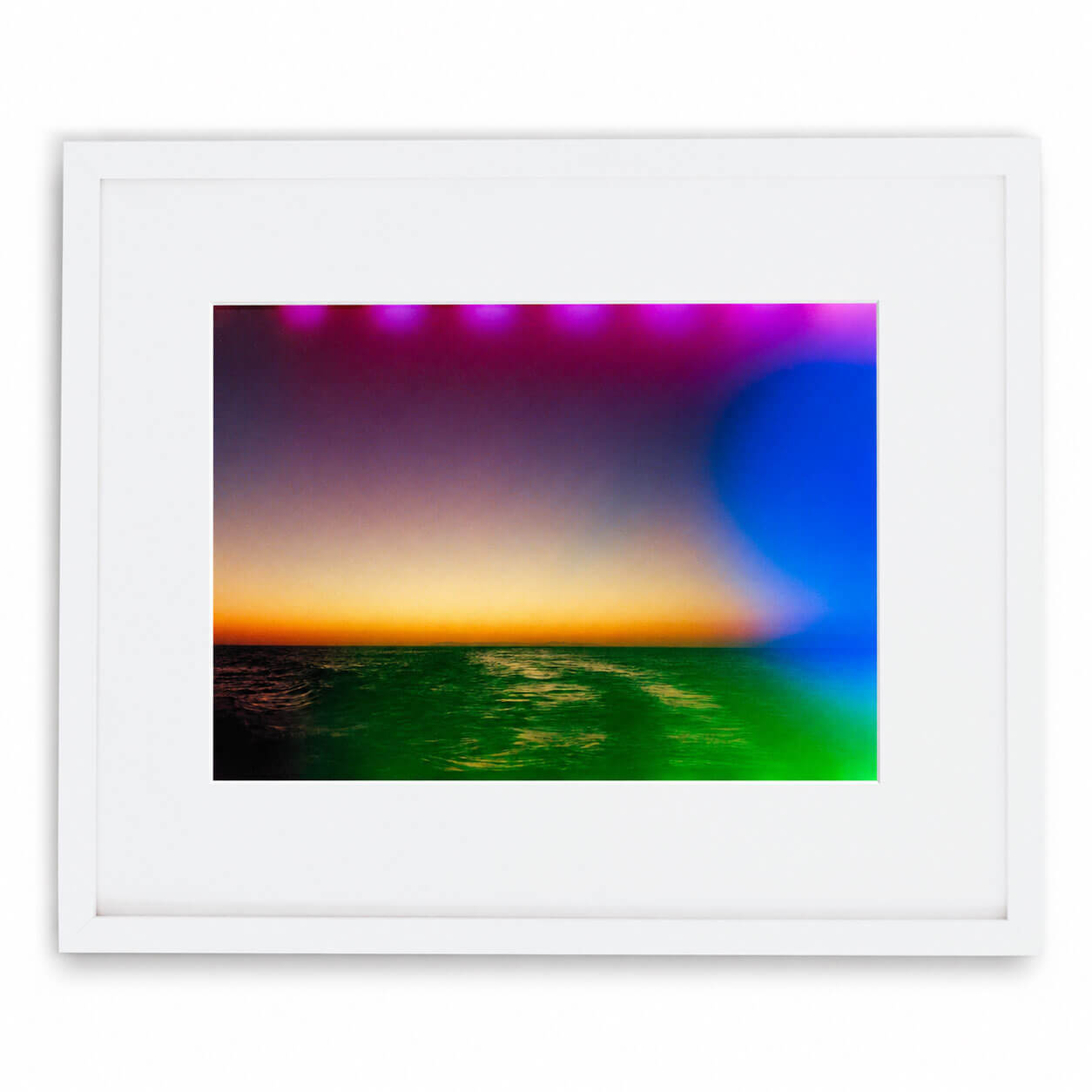 A framed art print featuring a colorful abstract sunset or sunrise over water, with a white frame and mat on a clean white background.